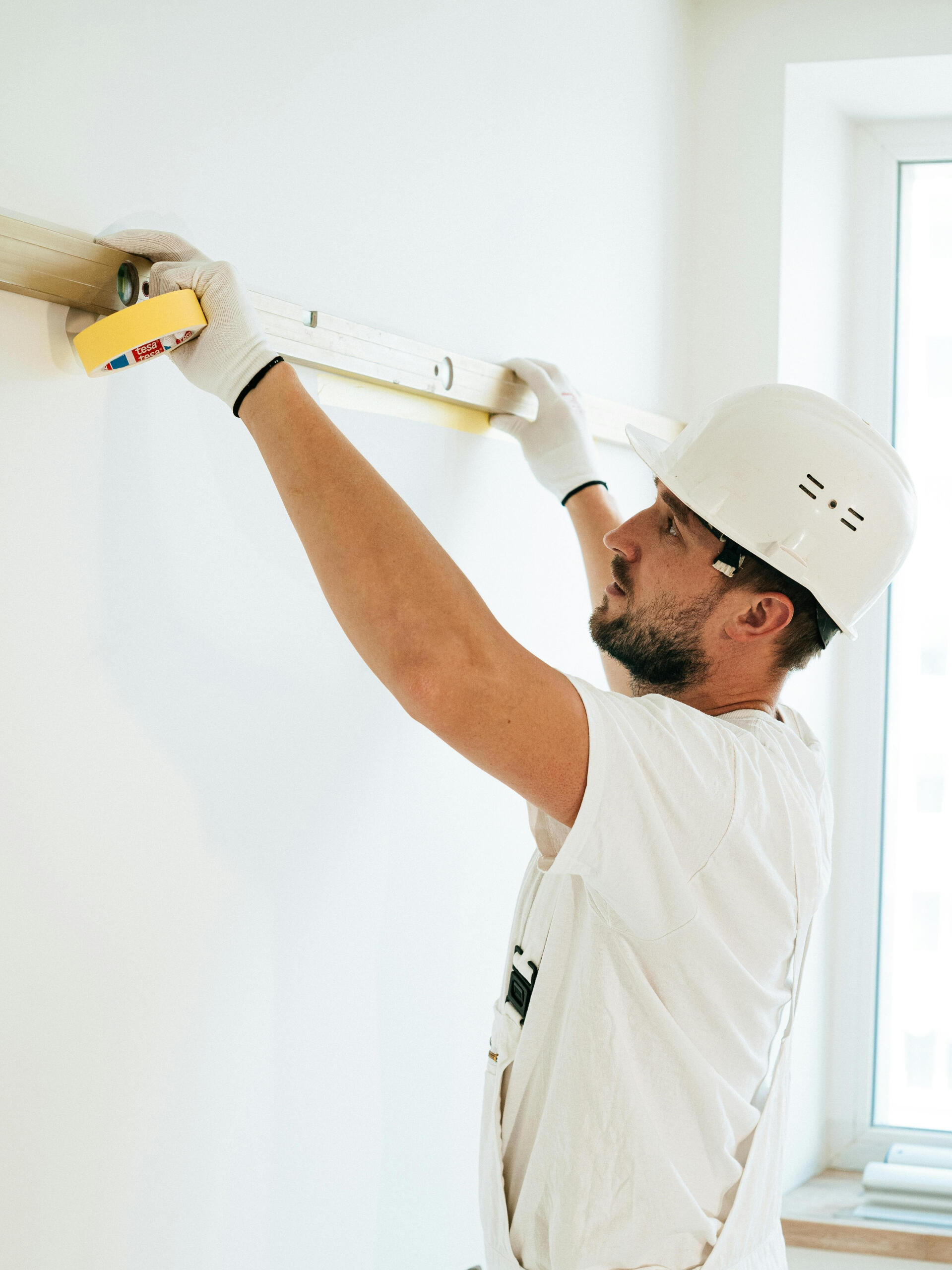 Handwerker misst Wand im Schlafzimmer mit Maßband und Lineal